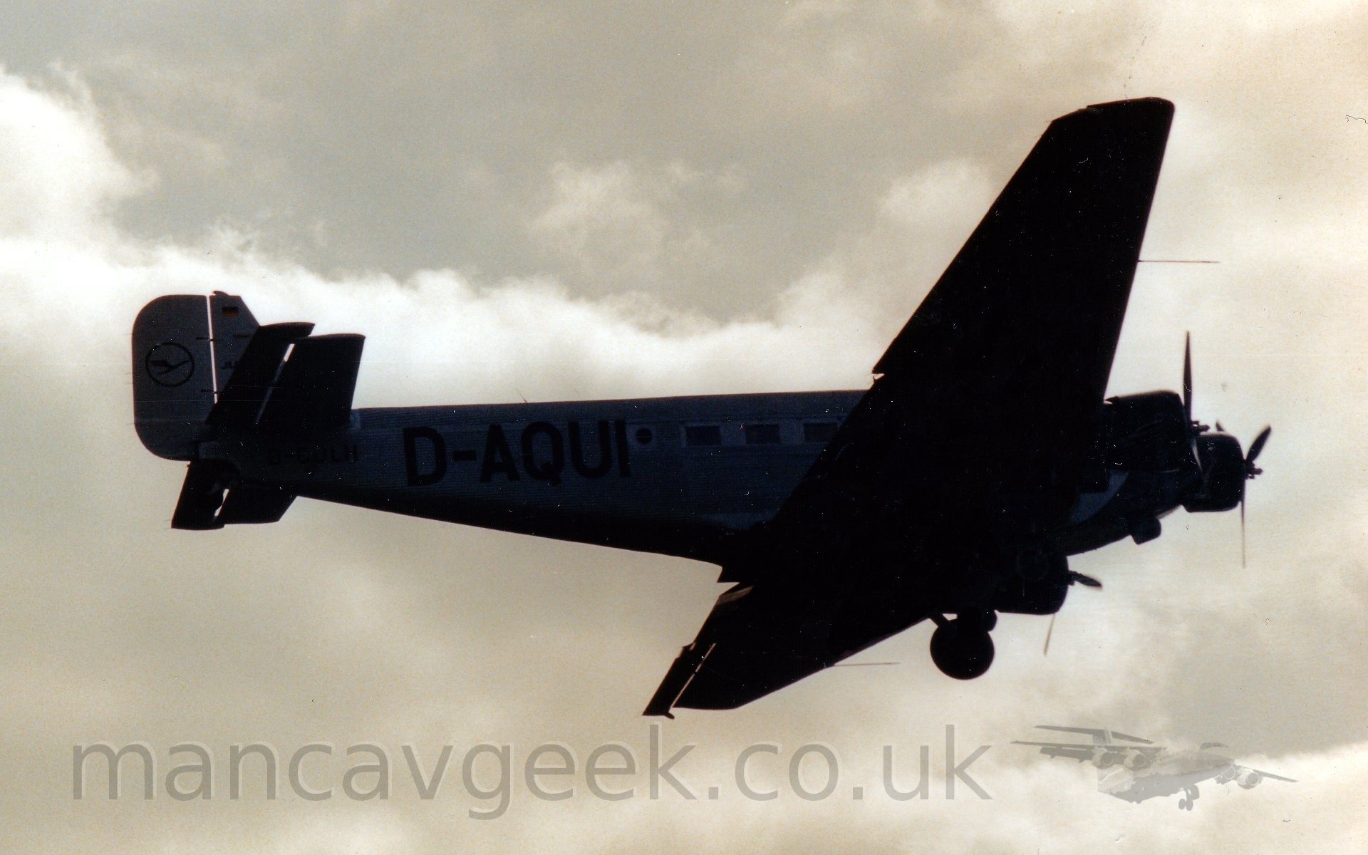 Heavily backlit shot of a 3 propellor-engined airliner flying from left to right at a low altitude, with it's fixed tail-wheel undercarriage in place (obviously), and flaps extended from the rear of the wings, suggesting it is about to land.
The fuselage is metallic grey, with a corrugated surface, and the black registration "D-AQUI" on the rear fuselage.
Dramatic grey sky fill the background. Heavily backlit shot of a 3 propellor-engined airliner flying from left to right at a low altitude, with it's fixed tail-wheel undercarriage in place (obviously), and flaps extended from the rear of the wings, suggesting it is about to land.
The fuselage is metallic grey, with a corrugated surface, and the black registration "D-AQUI" on the rear fuselage.
Dramatic grey sky fill the background.